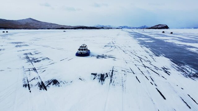 A hovercraft rides on the blue icy Lake Baikal covered with white snow, panoramic aerial shot