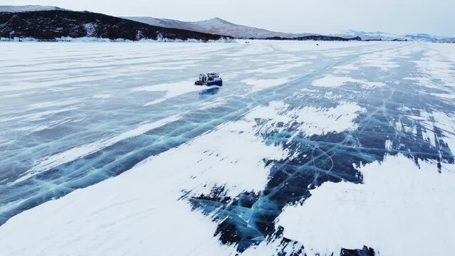 A hovercraft rides on the blue icy Lake Baikal covered with white snow, panoramic aerial shot