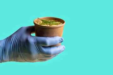 Chicken soup in a paper disposable Cup for taking out or delivering food in a man's gloved hand...