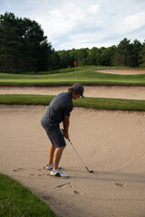 Male golfer in gray with ball in sand trap, bunker shot, multiple bunkers, end in sight, overcoming obstacles, challenging shot, target in sight