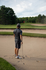 Male golfer in gray with ball in sand trap, bunker shot, multiple bunkers, hole in sight, overcoming obstacles, challenging shot