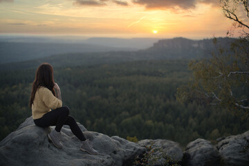Fototapeta premium Eine Frau genießt nach der Wanderung, vom Gipfel des Berges, die atemberaubende Aussicht der Landschaft mit einem wunderschönen Sonnenuntergang