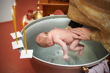 Priest baptizes the newborn by dipping him into the water