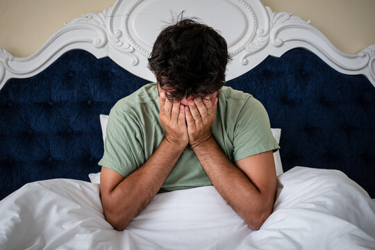 Hombre levantandose de la cama con depresi&oacute;n y malestar, cubriendose la cara con las manos