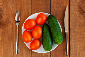 Cucumbers and tomatoes on a white plate. A plate with vegetables on the table. Diet food. Vegetarian food.