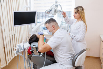 The dentist doctor looks at the patient's teeth and holds dental instruments near the mouth. The assistant helps the doctor. They wear white uniforms with masks and gloves. Dentist. Dental office