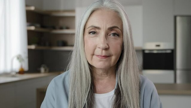 Portrait calm confident adult middle-aged woman pensioner granny mistress homeowner tender mature old lady with long grey hair posing in kitchen room serene looking at camera healthy beauty appearance