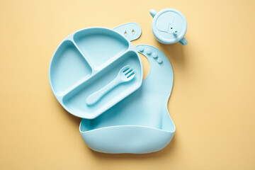 Silicone baby feeding supplies set. Top view silicone bib, plate with fork, sippy cup on pastel...
