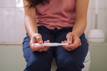 Woman holding positive pregnancy test at bathroom