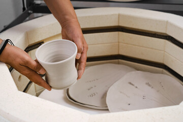 close-up of hands putting vase into the kiln, oven for roasting of unbaked clay handmade products,...