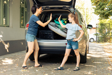 Woman and young child doing highfive before leaving on holiday trip at seaside, loading baggage and...