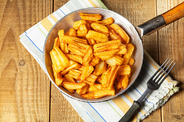 French fries on old pan placed on wooden table.