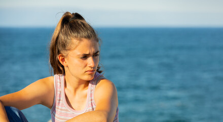 young girl in a tank top with a pensive look and the sea in the background with a copy space