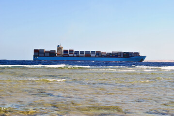 A huge container ship carries many commercial containers. Side view from the shore