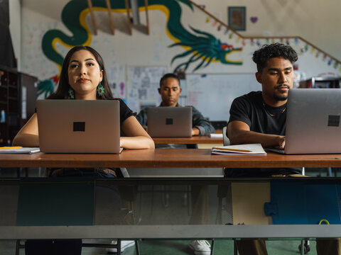 Native girl looks up while 2 native boys work on their laptops in school