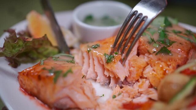 closeup of hand cutting roasted salmon steak on white plate with wok vegetable