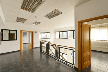 Empty offices with gray stoneware floors, metal railing, wood and glass of stairs and entrances to...