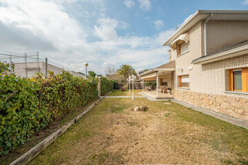 Plot with garden and fence covered with vines in a single-family house made of stone and white brick