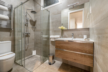 Bathroom with marble tiles, wooden cabinet with drawers, shower cabin with glass partitions and...