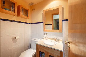 White tile and orange paint bathroom with white porcelain sink, matching wood cabinets, wood framed mirror