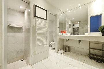 Fototapeta na wymiar Large bathroom tiled with white marble, countertop with two sinks, large mirror covering one wall and separate cubicles for shower and toilet