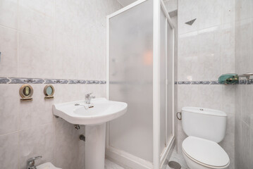 Tiled bathroom with gray trim, white porcelain sink with matching pedestal, and shower stall with white aluminum trim
