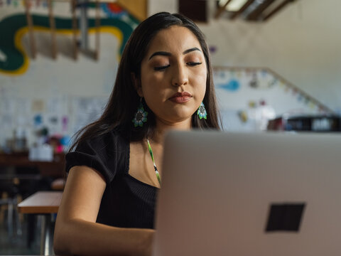 Close up of a native girl with beaded earrings typing on her laptop in the classroom