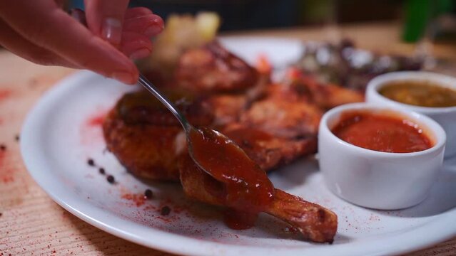 closeup of hand adding tomato sauce on roasted chicken tabaka on white plate