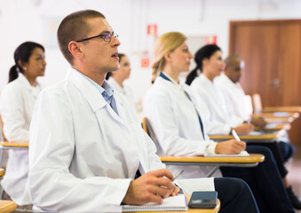 Portrait of confident man doctor listening to lecture within refresher course. Professional development concept