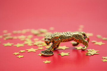 A bronze figure of a tiger with a coin - the symbol of financial well-being and wealth on a red...