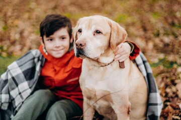 Love to the animals. Raising children to be kind. A boy walks with his labrador retriever in the park in autumn.