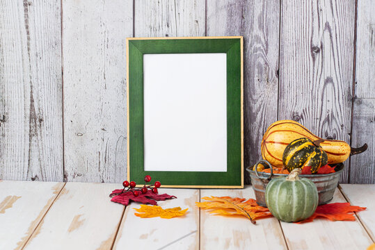 Mock up green frame with autumn leaves and pumpkins on a wood shelf. fall concept. Portrait frame against a white wall. copy space