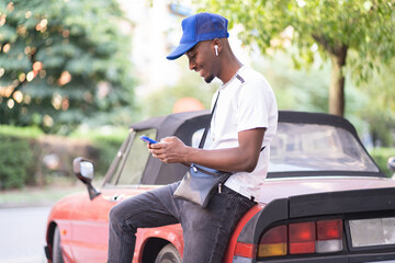 giovane ragazzo nero appoggiato su un auto sorride mentre usa il suo smartphone