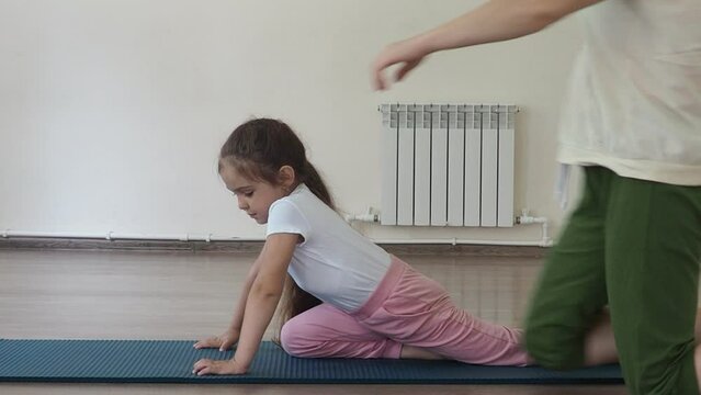 girl child is engaged in gymnastics, dancing, sports, yoga and stretching with a trainer in the gym. Girl in sportswear on a sports mat doing exercises. charming little doing yoga in fitness hall