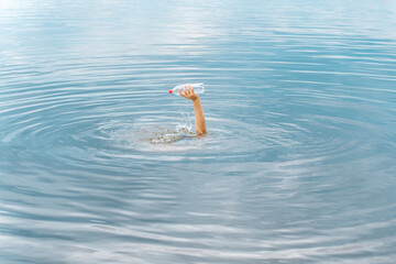 Raised arm holding bottle plastic garbage beach pollution ocean plastic waste ocean trash sea waste. Emerging from water plastic bottle raised hand trash beach. Motivation concept hand trash clean up