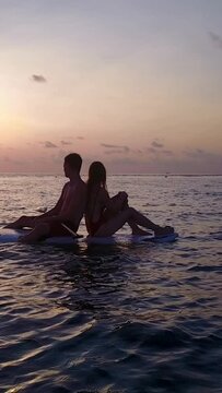 Young couple relaxing on a surfboard in the sea at sunset