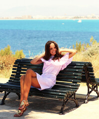 Cute girl sitting on a bench. Relaxed atmosphere. Thoughtful girl by the sea. Cinematic Film-Like. Cute charming girl, Spain, Mallorca. Attractive brunette with curly