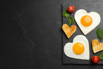 Heart shaped fried eggs and toasts on black table, top view. Space for text