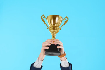 Businessman holding gold trophy cup on light blue background, closeup
