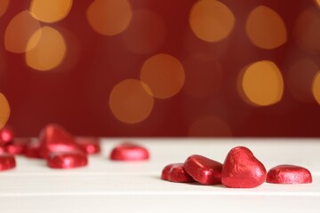 Heart shaped chocolate candies on white table against blurred lights, space for text. Valentines's day celebration