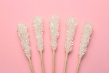 Wooden sticks with sugar crystals on pink background, flat lay. Tasty rock candies