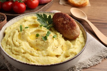 Bowl of tasty mashed potatoes with parsley, black pepper and cutlet served on wooden table, closeup