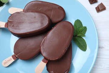 Plate with glazed ice cream bars and fresh mint on white wooden table, top view