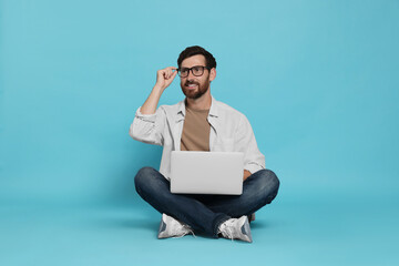 Handsome man with laptop sitting on light blue background