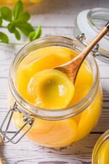 sweet canned yellow peach with spoon in glass jar on table
