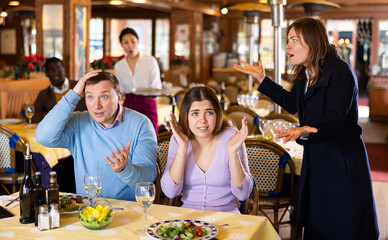 Woman quarreling with her husband who dating in restaurant with young mistress.