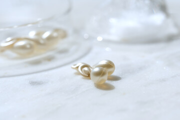 Serum capsules in petri dish for healthy skin with ice balls. Orange semitransparent capsules. Anti-wrinkle rejuvenation skin treatment. Beauty product presentation. Off white stone marble background.