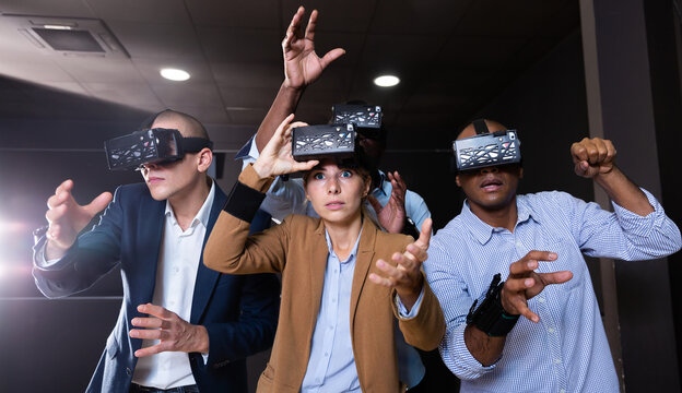 Portrait of group of young adult people with virtual reality goggles gesturing standing in dark room