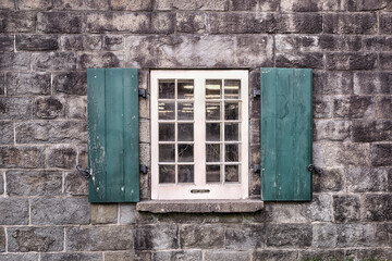 Old simple window with opened wooden green shutters. Aged stone wall building in background.