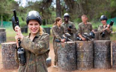 Fototapeta premium Happy woman and her paintball sport team in protective uniform at shooting range